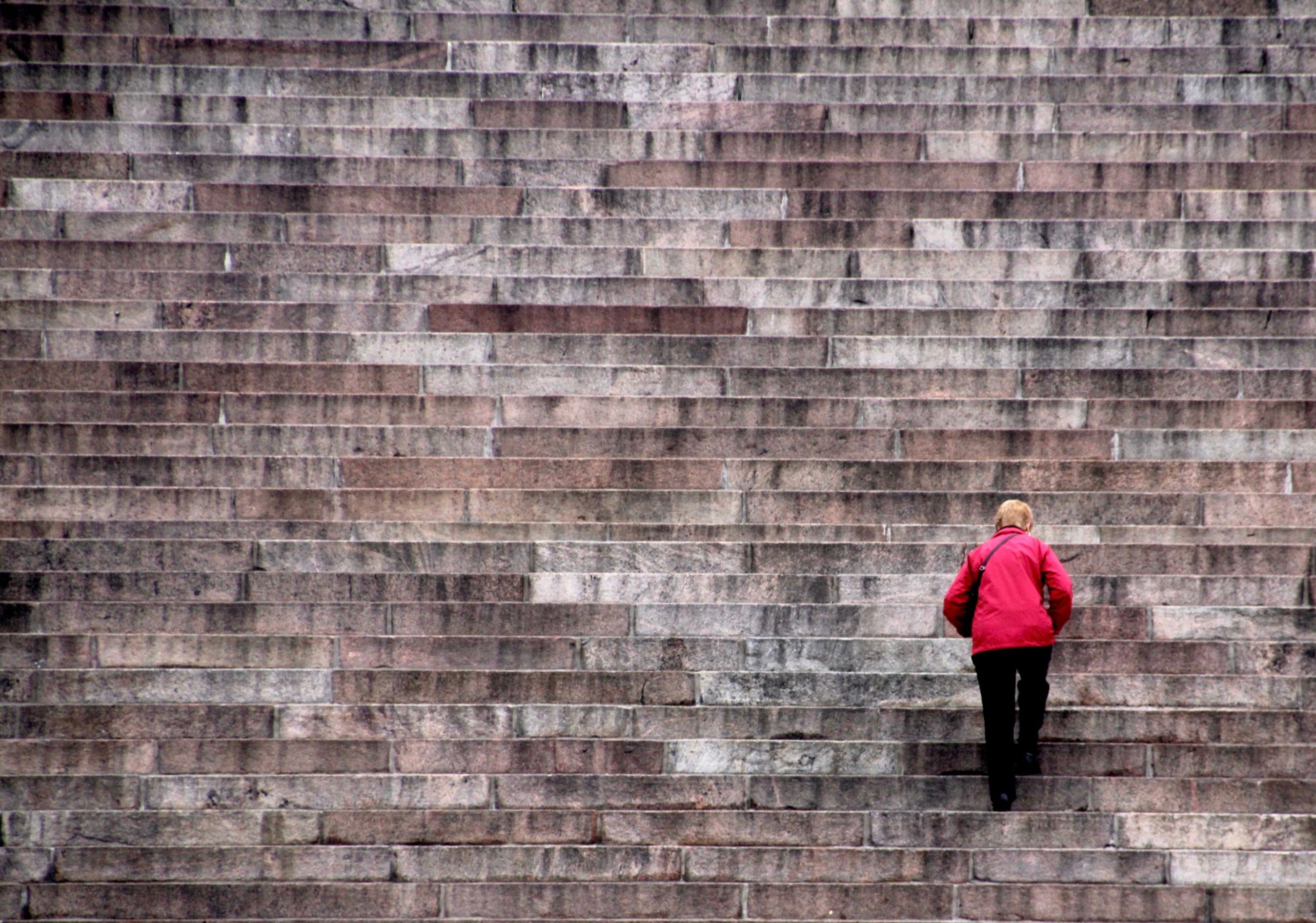 A person in a red jacket climbing a long flight of stone steps